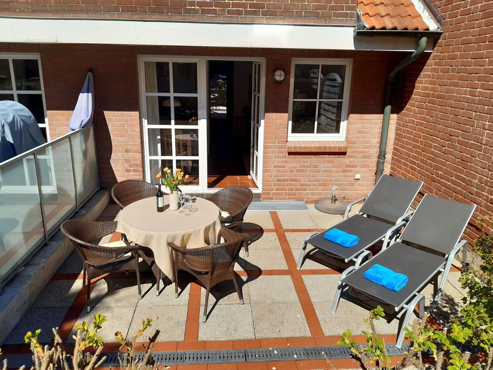 Terrasse mit Tisch, Stühlen und Liegestühlen. Hintergrund: rote Ziegelwand und Fenster.