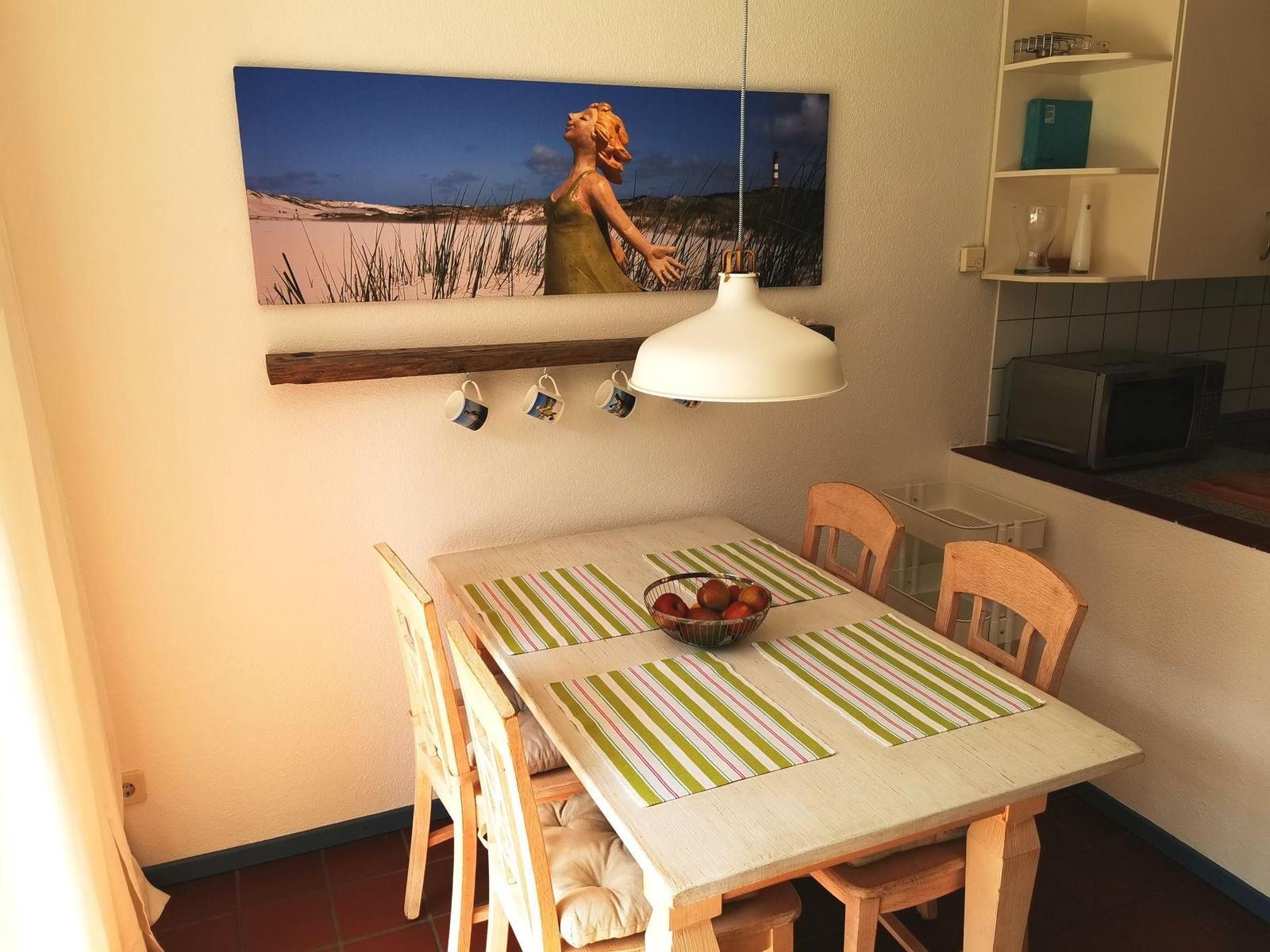 Esszimmer mit Tisch, Stühlen und Wandbild. Mikrowelle und Küchenzeile sichtbar.
