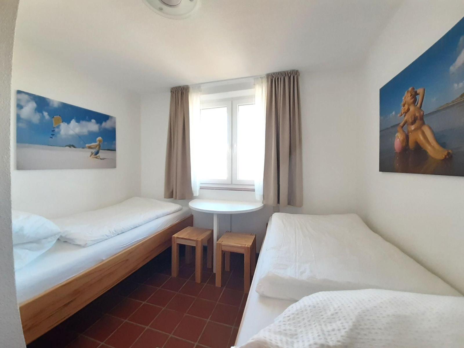 Zwei Betten, Tisch mit Stühlen, Fenster mit Vorhängen, Wandbilder