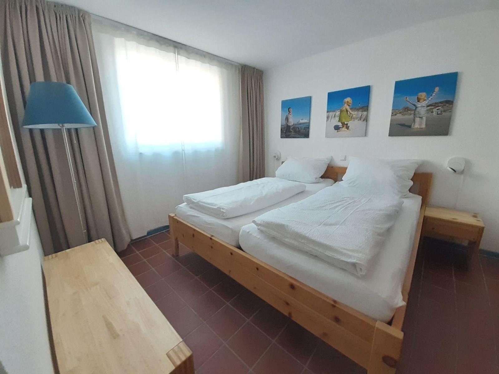 Schlafzimmer mit Doppelbett, Holzmöbel und Fenster mit Vorhängen.