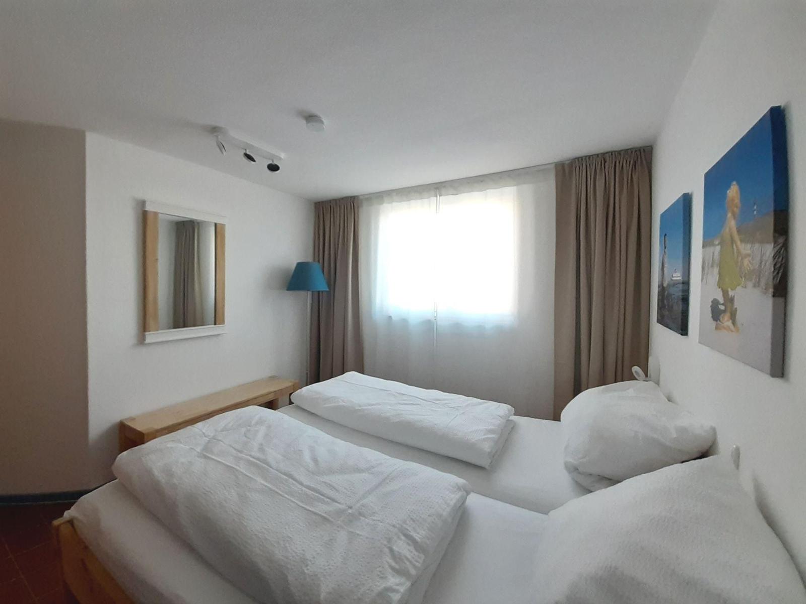 Zimmer mit Doppelbett, Fenster, Vorhängen und Wandbildern.