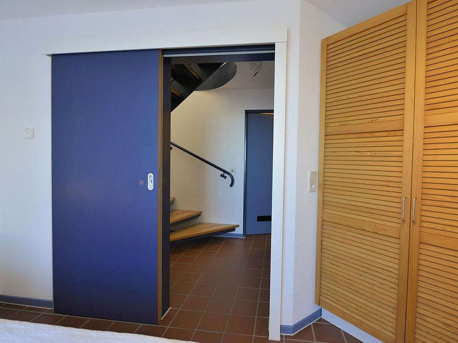 Schlafzimmer mit Schiebetür und Holzschrank. Treppenhaus im Hintergrund.