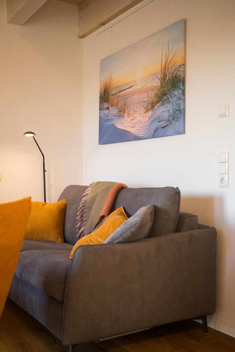 Ein grauer Sofa mit Kissen und Decke unter einem Wandbild.
