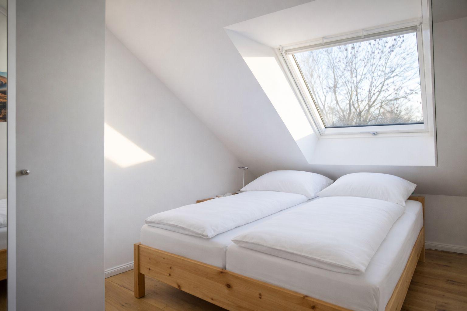 Schlafzimmer mit Dachschrägen, Doppelbett und Dachfenster.