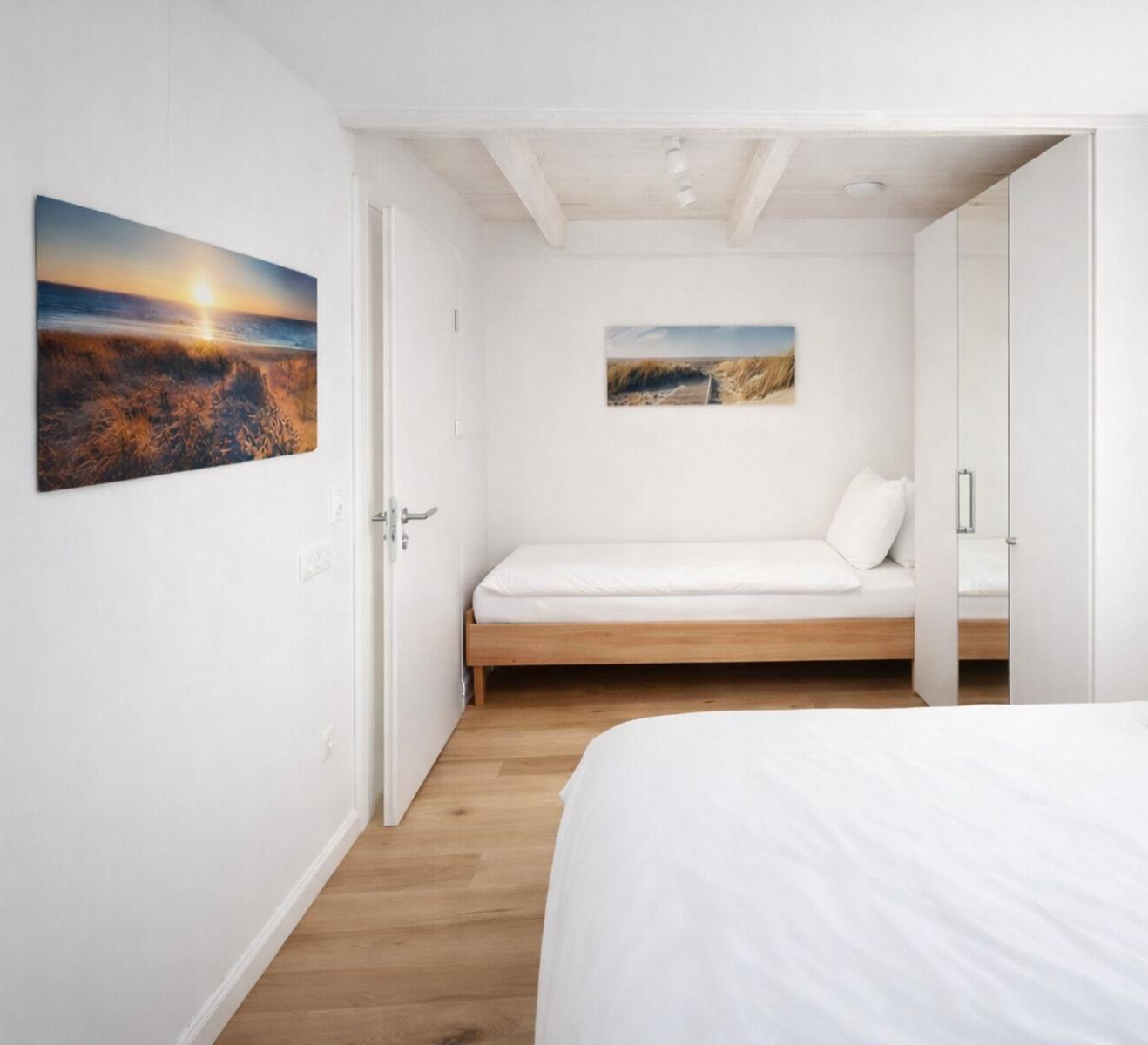Schlafzimmer mit Bett, Wandbild und Holzboden. Durchgang zu einem weiteren Raum.