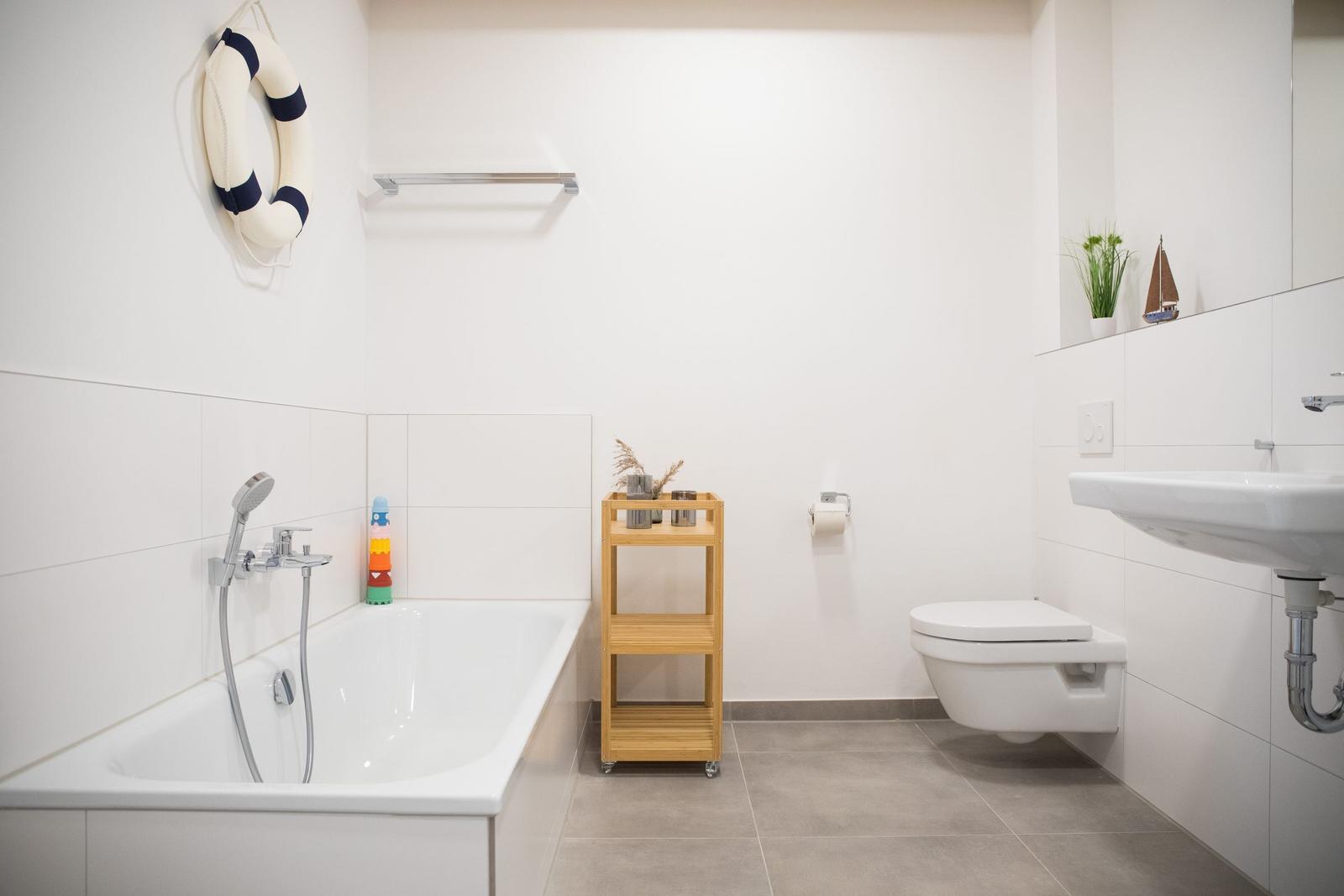Badezimmer mit Badewanne, Toilette und Waschbecken. Dekorative Elemente wie Rettungsring und Segelboot.