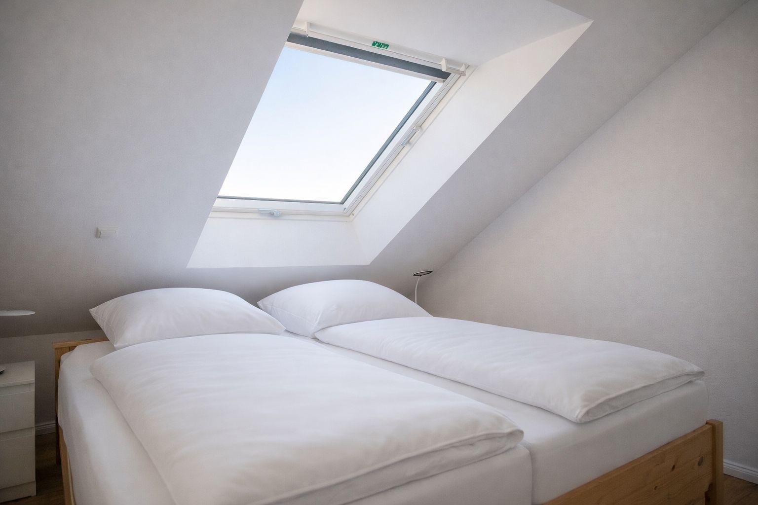 Schlafzimmer mit Dachschrägen und Dachfenster. Bett mit weißer Bettwäsche.