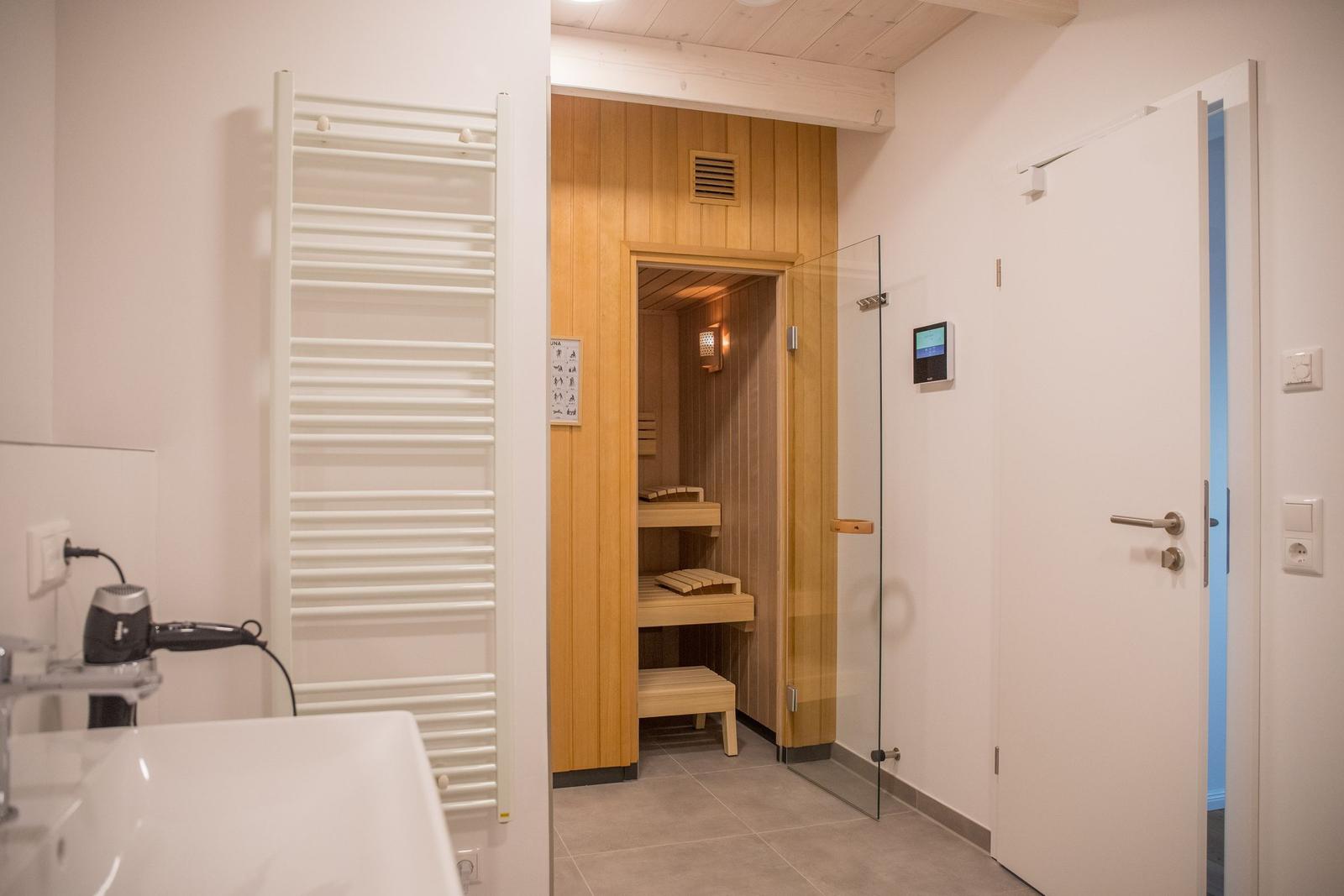 Dusche mit Glaswand, Sauna mit Holzverkleidung und Duschbereich mit Heizkörper.
