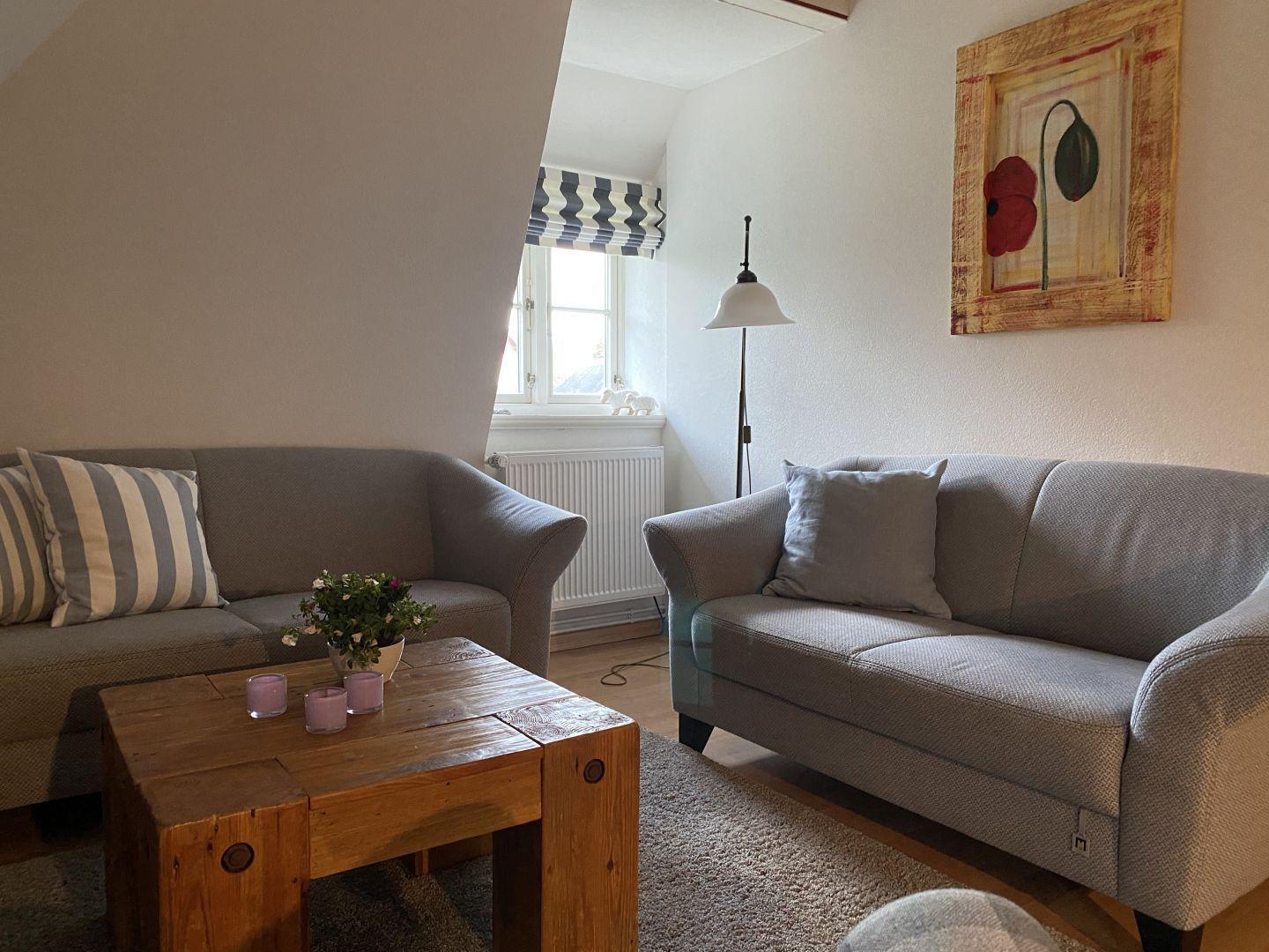 Zwei Sofas, Holztisch, Wandbild und Fenster mit Rollladen.
