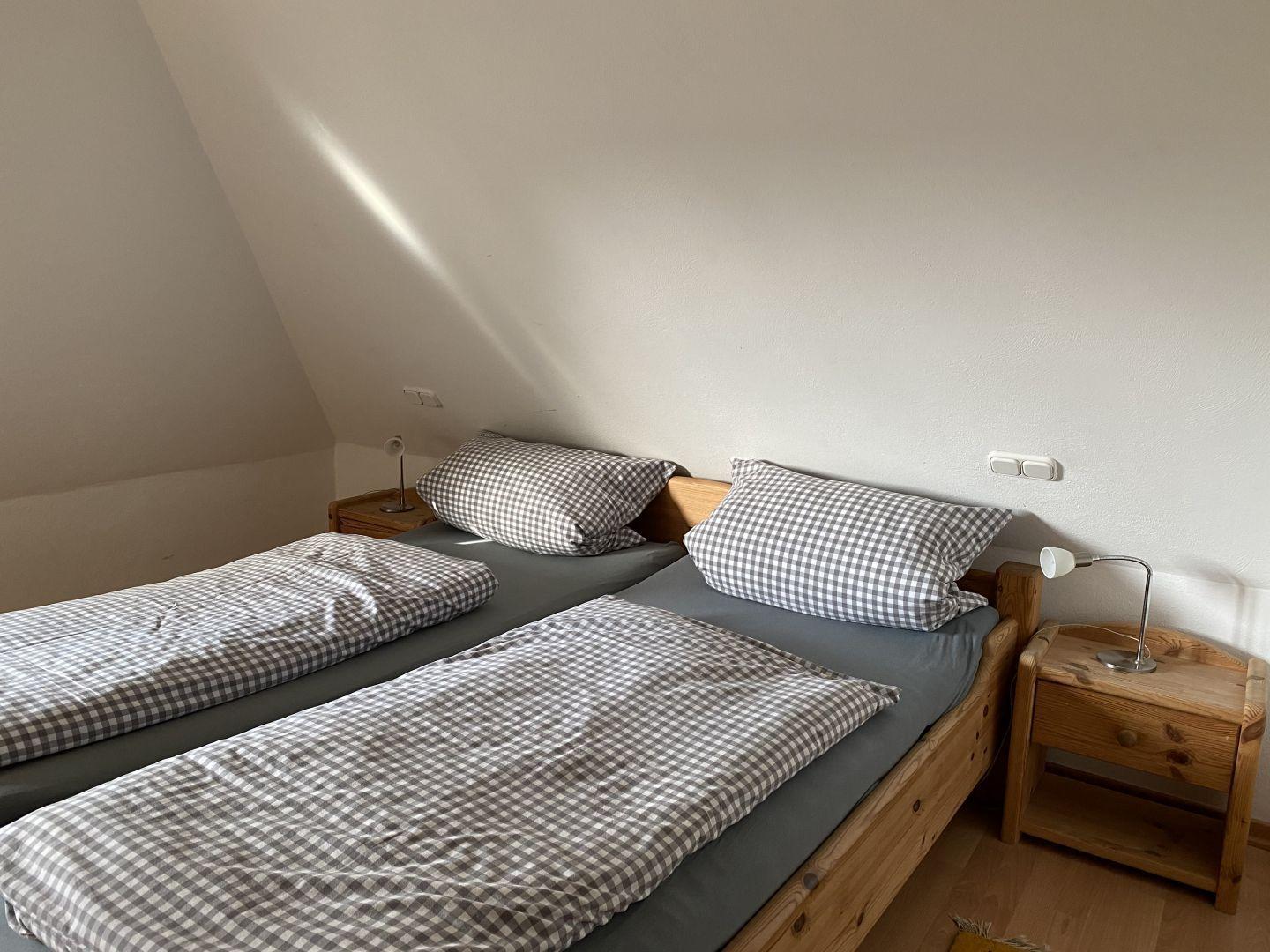 Zimmer mit zwei Einzelbetten, Holzgestell und Nachttischen mit Lampen.