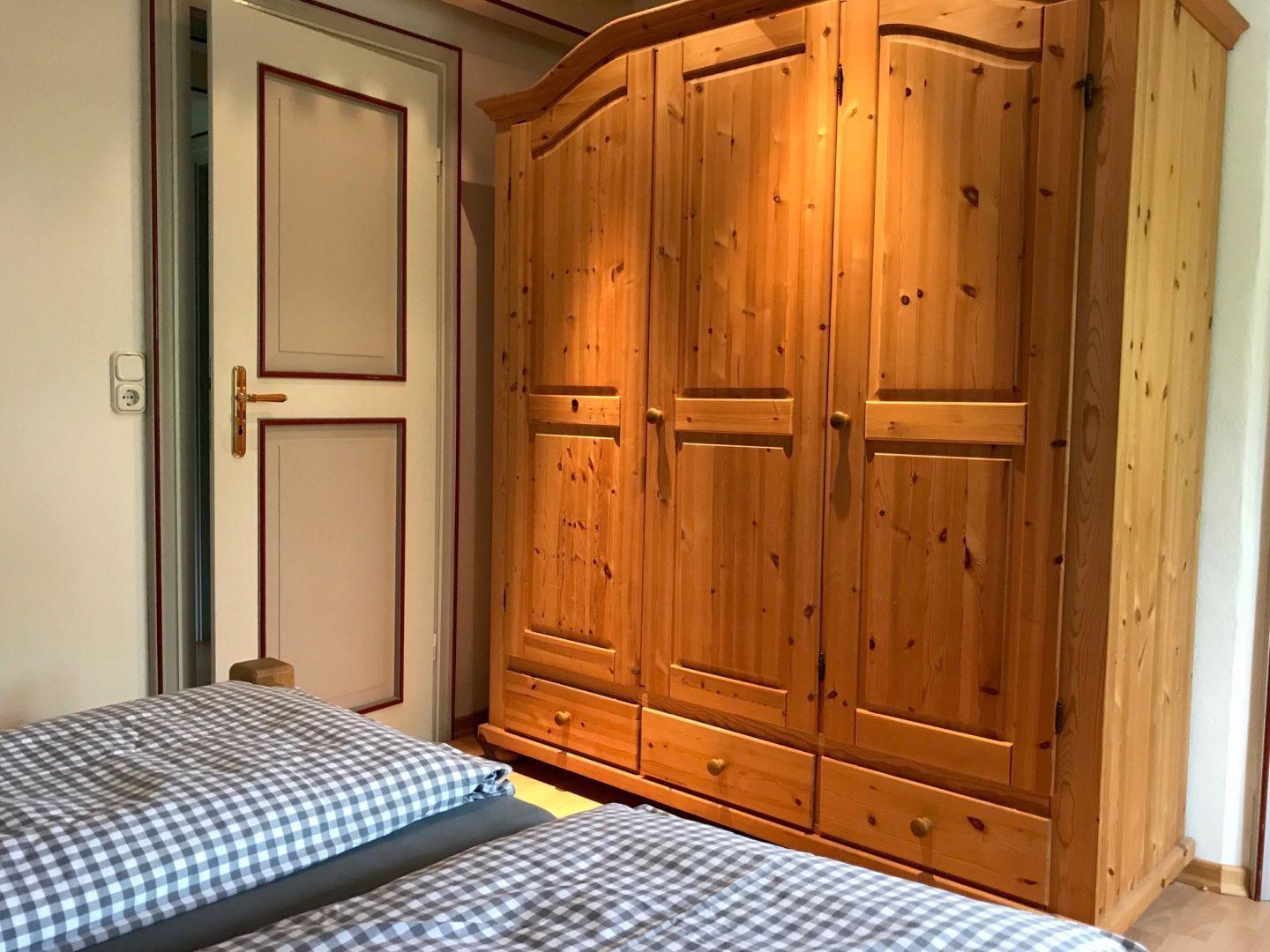 Schlafzimmer mit Holzschrank und Bett mit kariertem Bettzeug.