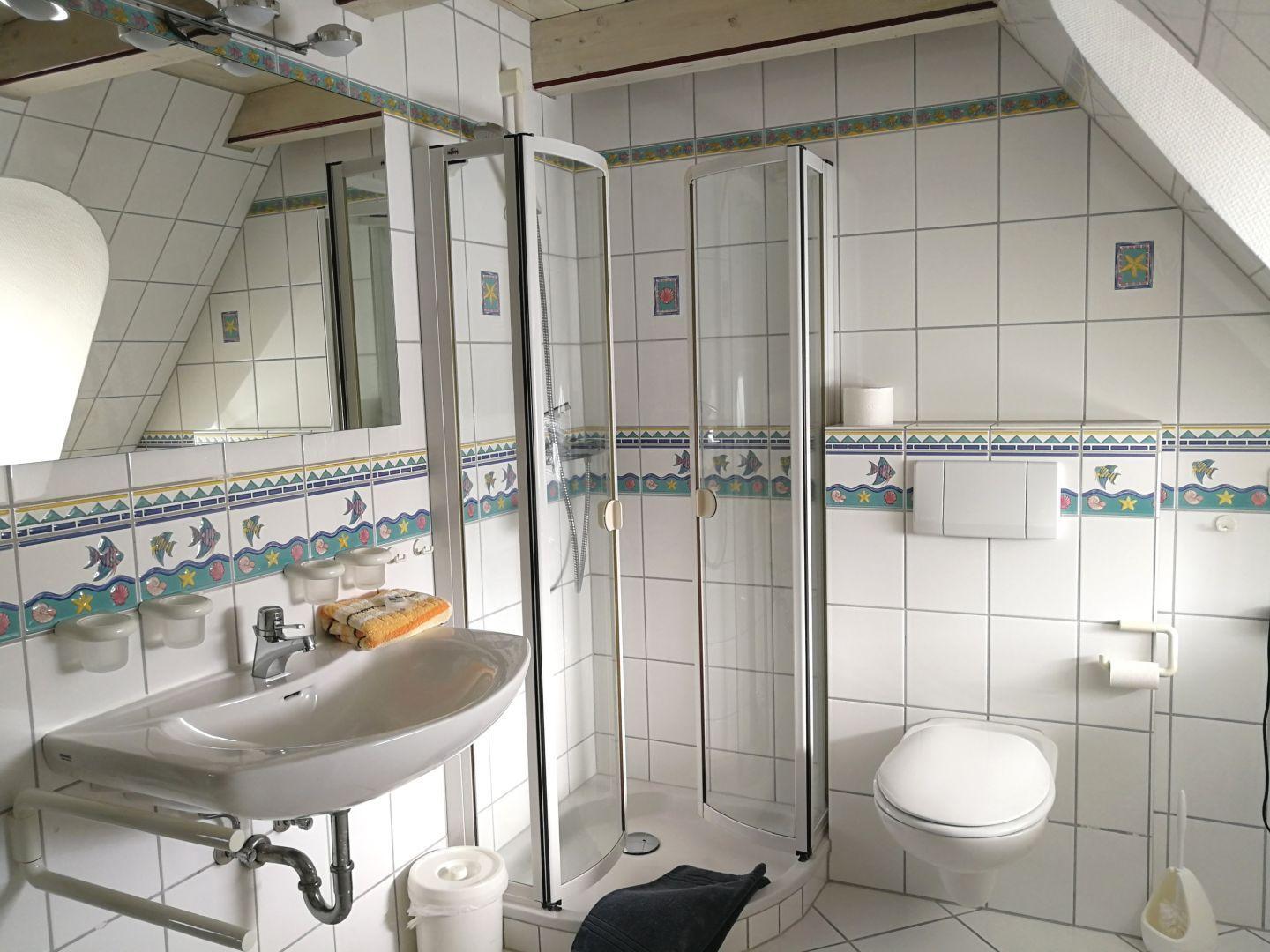 Badezimmer mit Dusche, Waschbecken und WC. Wandfliesen mit Meeresmotiven.