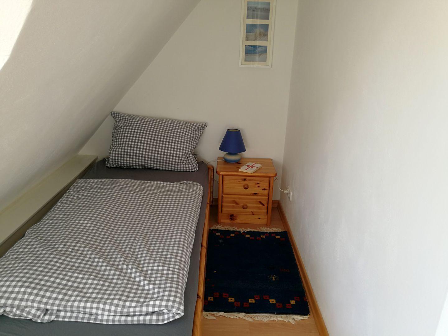 Ein Schlafzimmer mit Dachschräge, Bett, Nachttisch und Teppich.