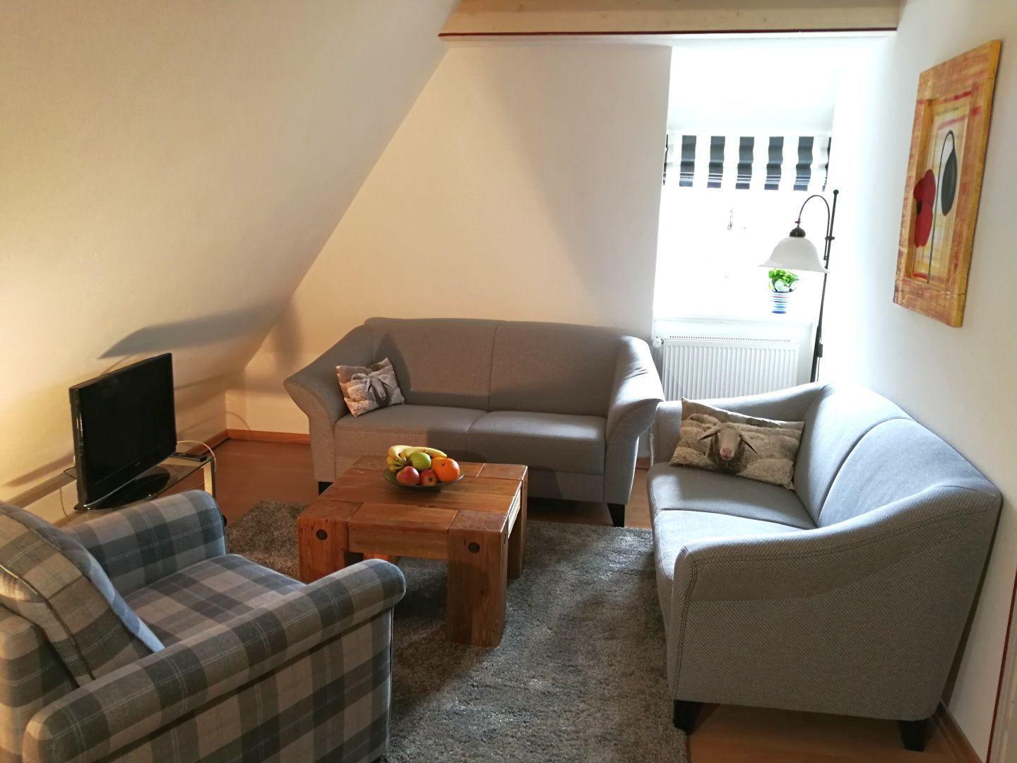 Wohnzimmer mit Sofa, Sessel und Holztisch. Fenster mit Jalousie und Wandbild.