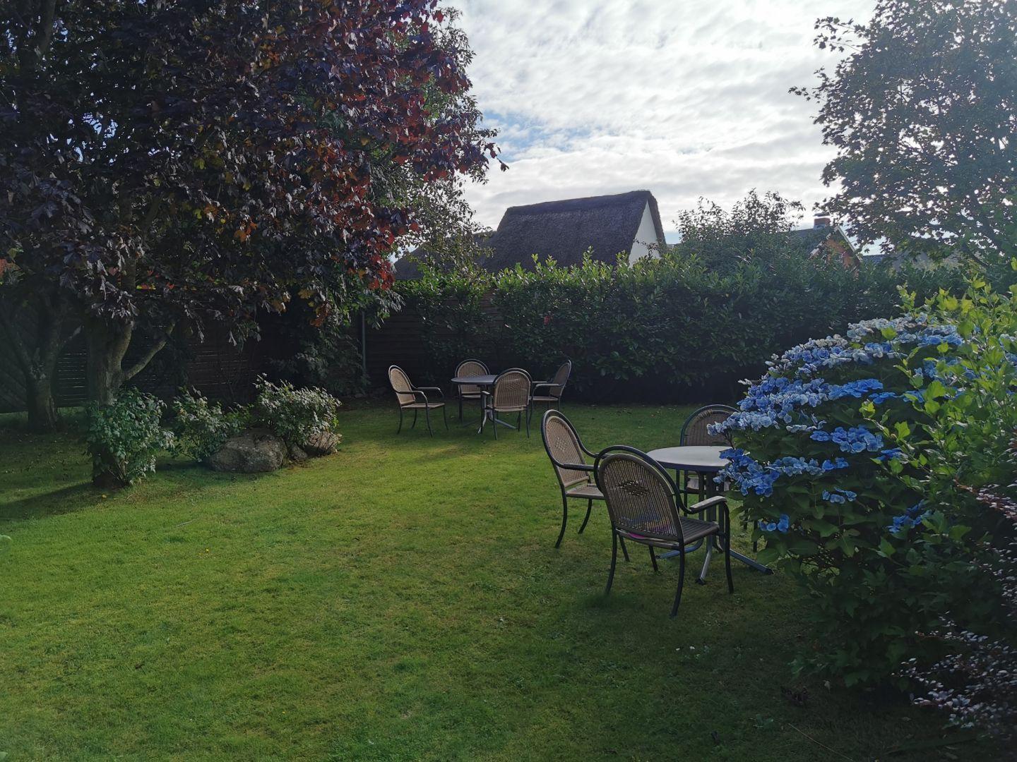 Garten mit zwei Tischen, Stühlen, Blumen und einem Blick auf ein Haus.