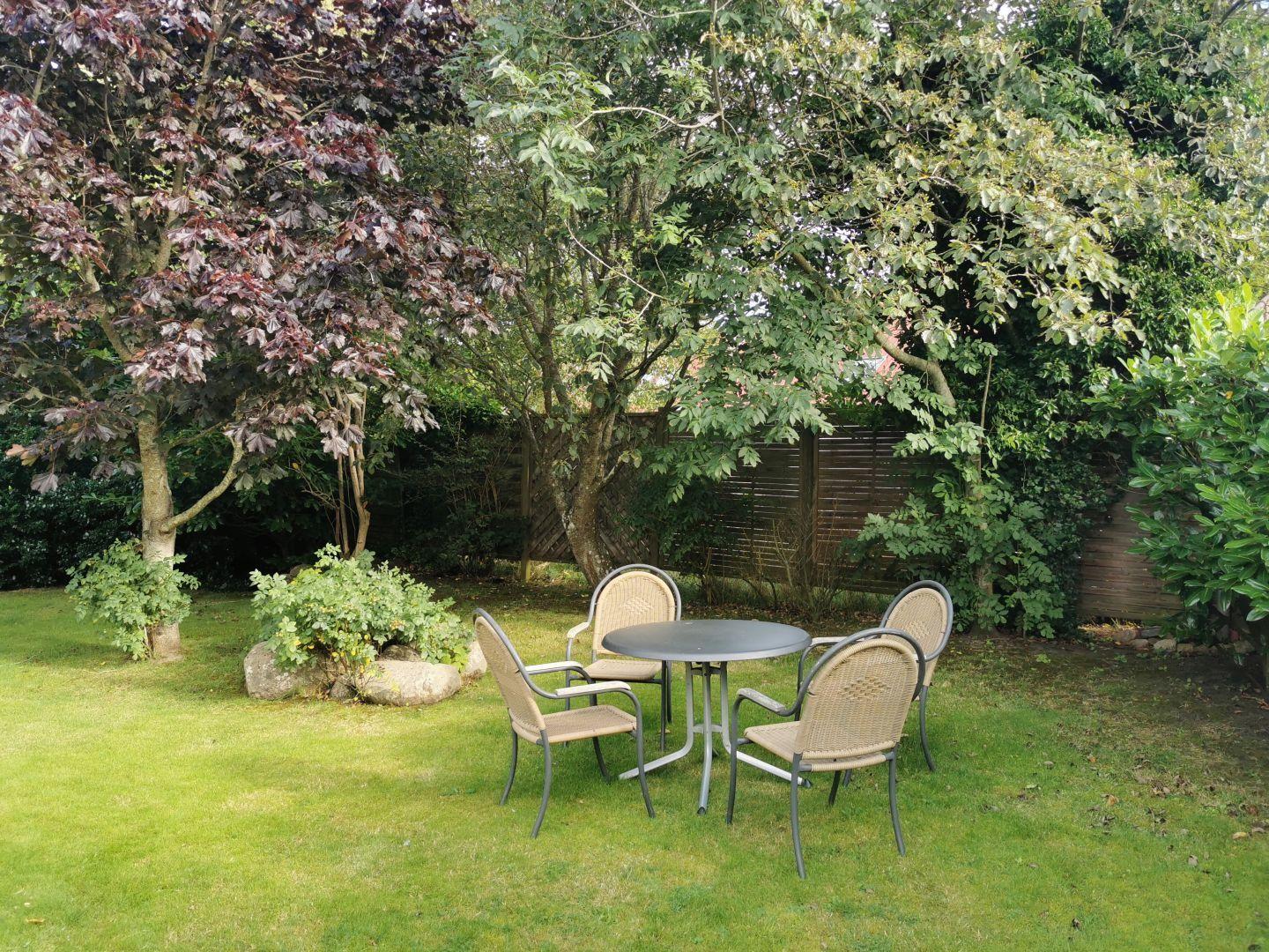 Garten mit runden Tisch und vier Stühlen unter Bäumen.