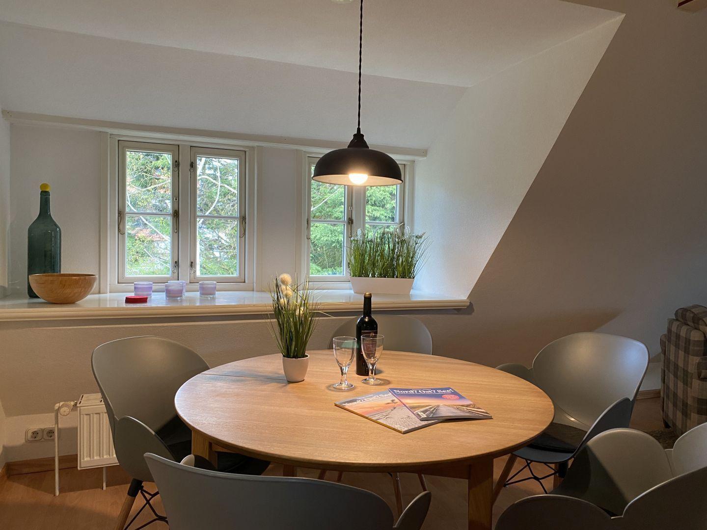 Rundes Esszimmer mit Tisch, Stühlen und Fensterblick auf Grün.
