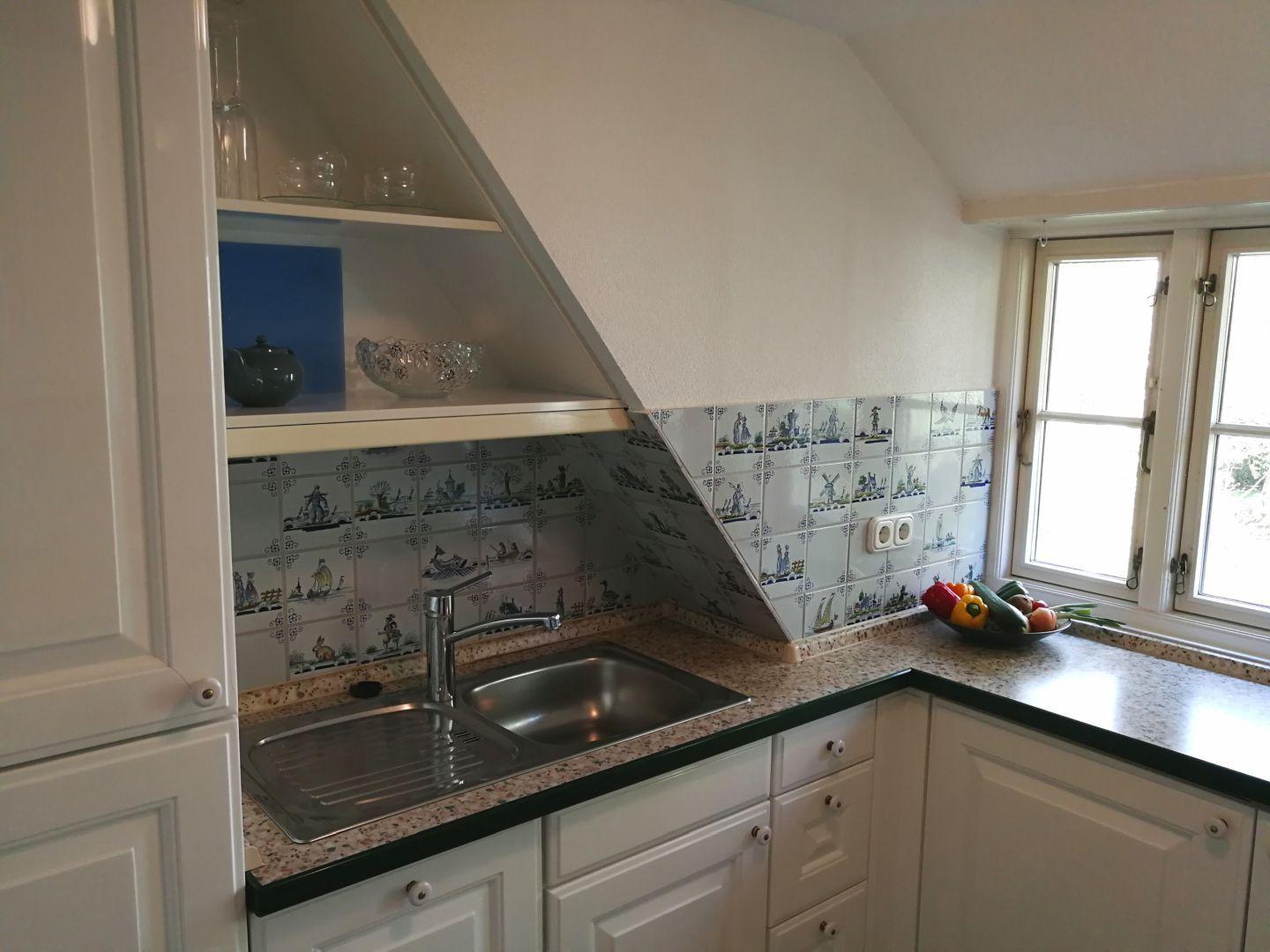 Küche mit weißen Schränken, Mosaikfliesen und Fenster.