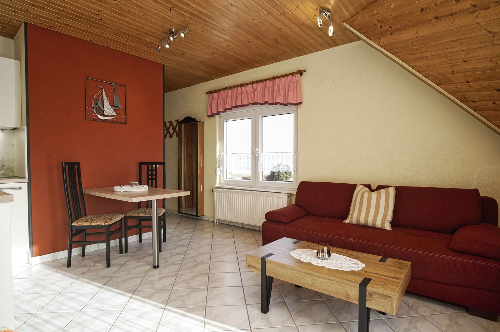 Wohn- und Essbereich mit Sofa, Tisch, Fenster und Holzdecke.