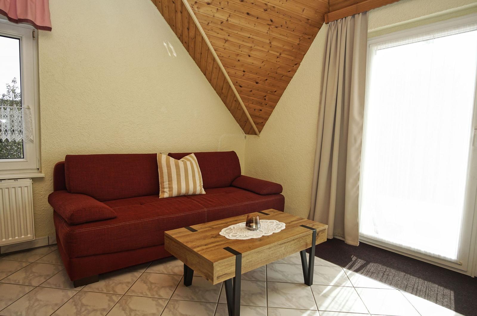 Ein Wohnzimmer mit rotem Sofa, Holztisch und schrägen Holzwänden.