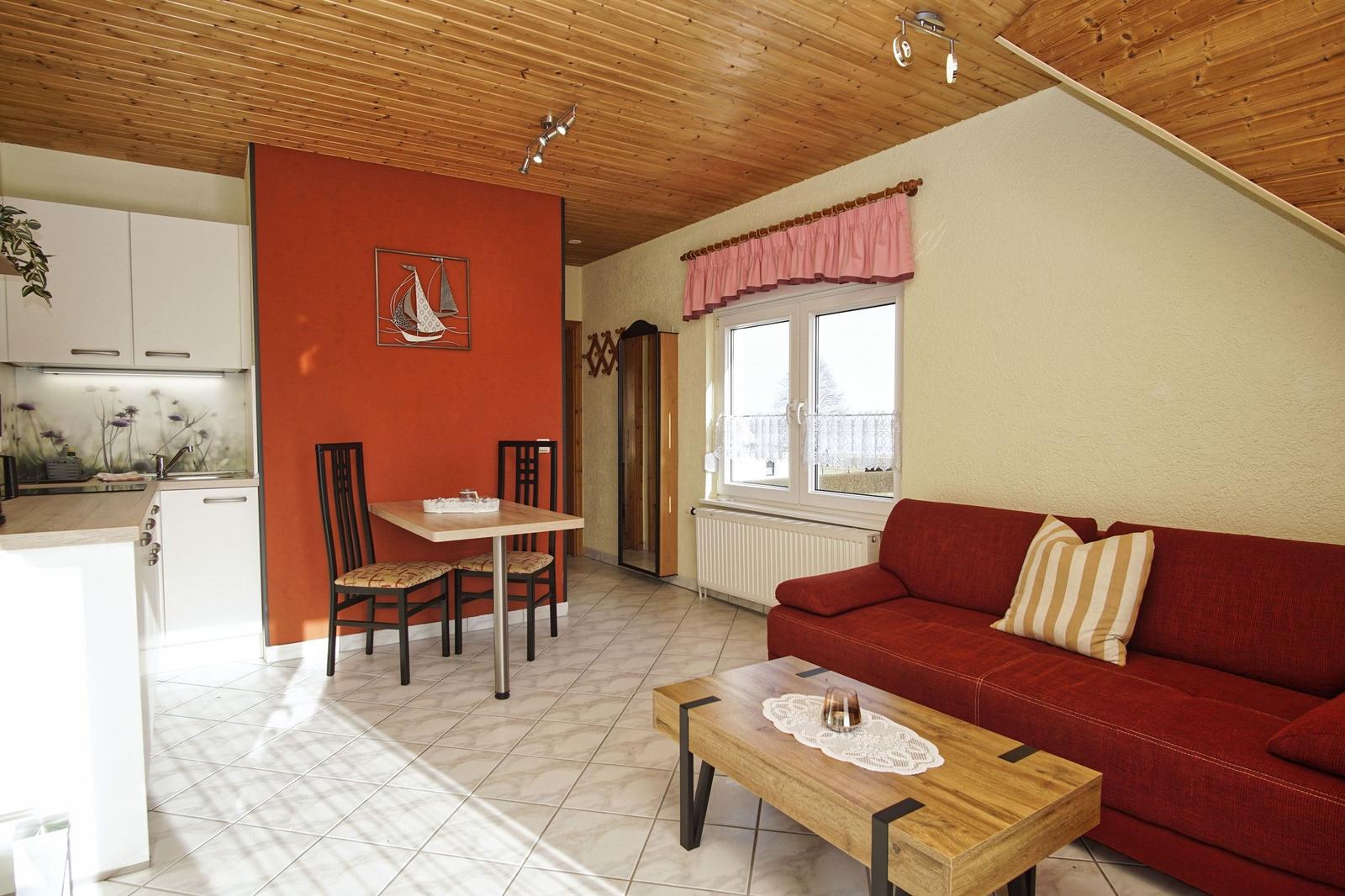 Wohnbereich mit Sofa, Tisch und Küchenzeile unter Holzdecke.