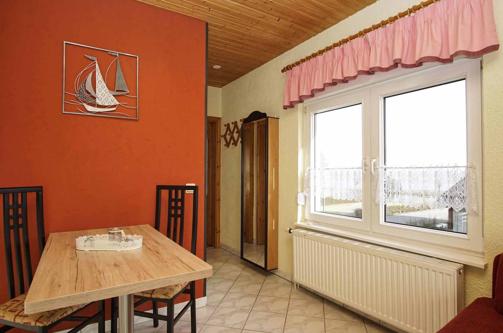 Esszimmer mit Tisch, Stühlen und Fenster mit Vorhängen.