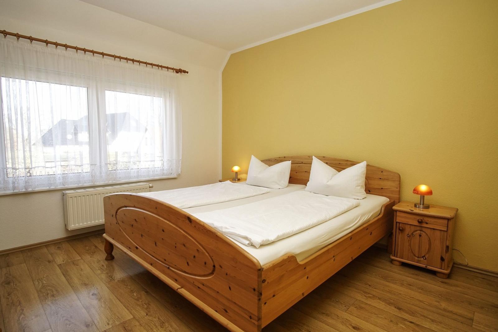 Ein Schlafzimmer mit Holzbett, Nachttisch und Fenster mit Vorhängen.