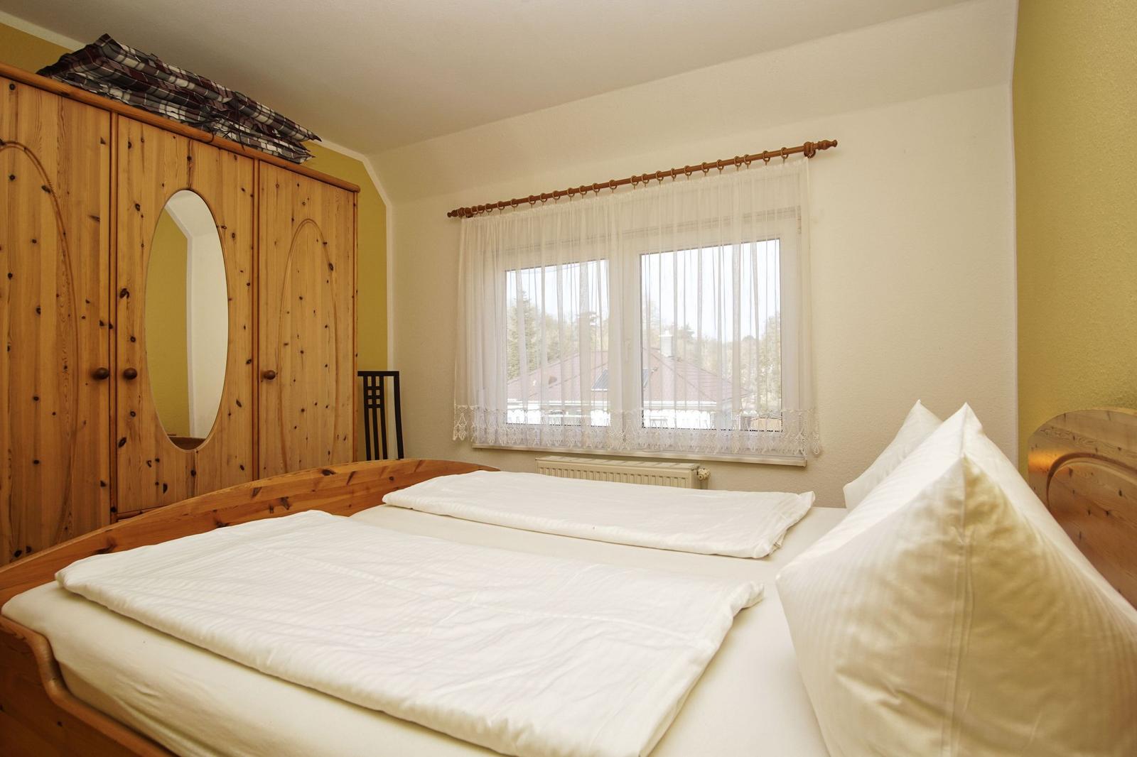 Schlafzimmer mit Holzbett, Kleiderschrank und Fenster mit Vorhängen.