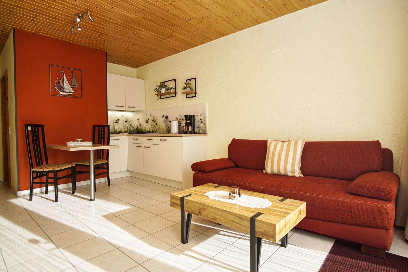 Wohnküche mit rotem Sofa, Holztisch und Küchenzeile.