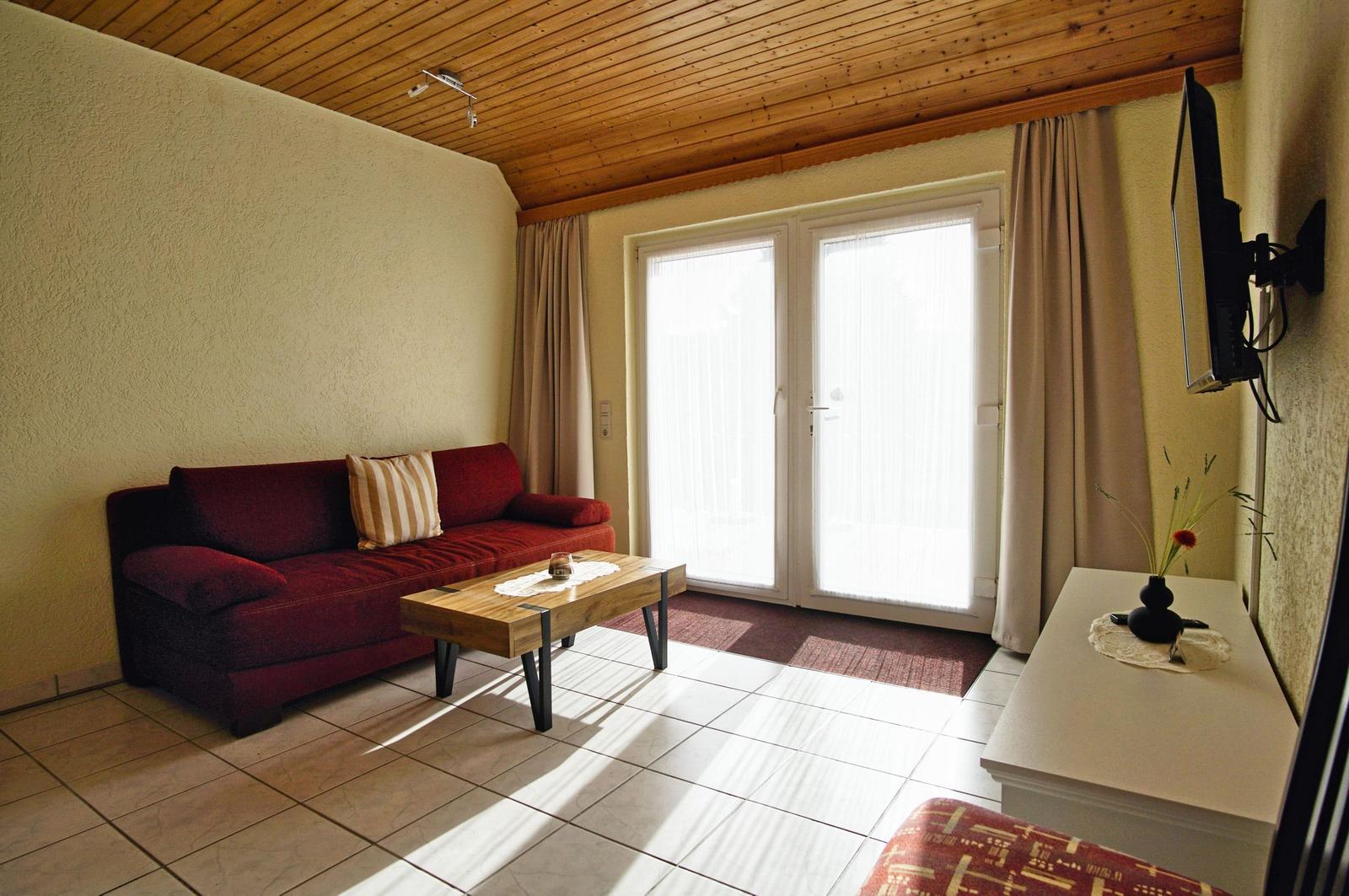 Wohnzimmer mit Sofa, Couchtisch und TV. Fenster mit Vorhängen.