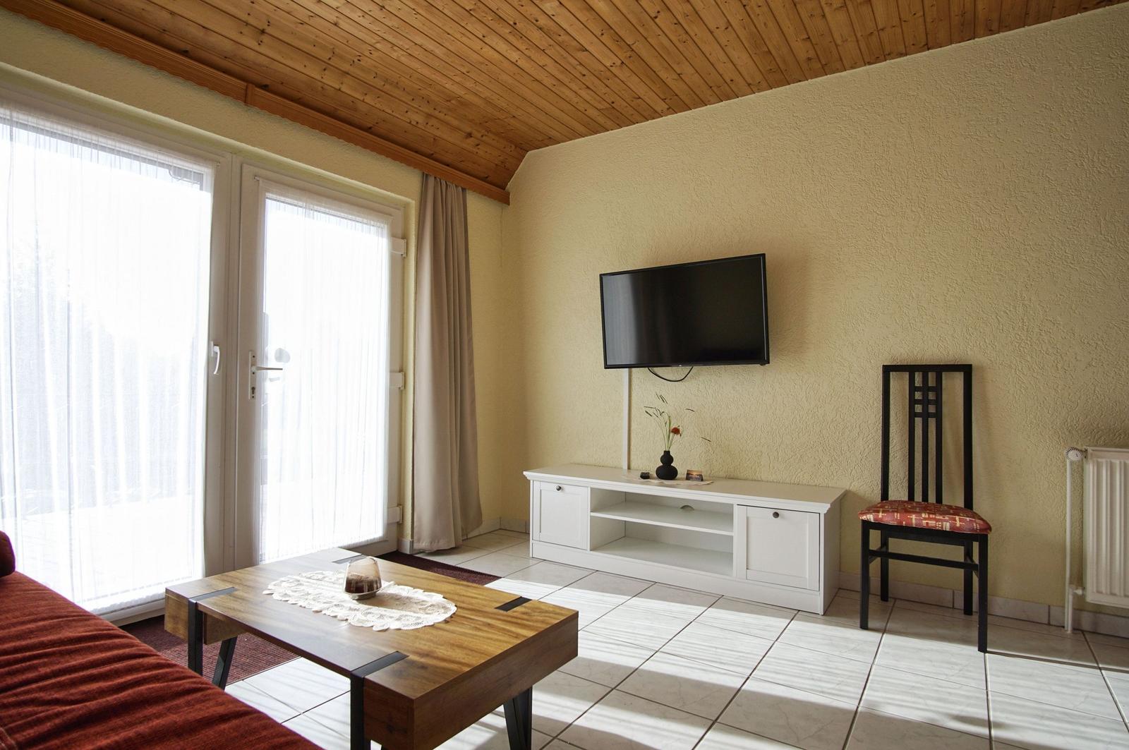 Wohnzimmer mit TV, Tisch, Stuhl und Fenster zur Außenseite.