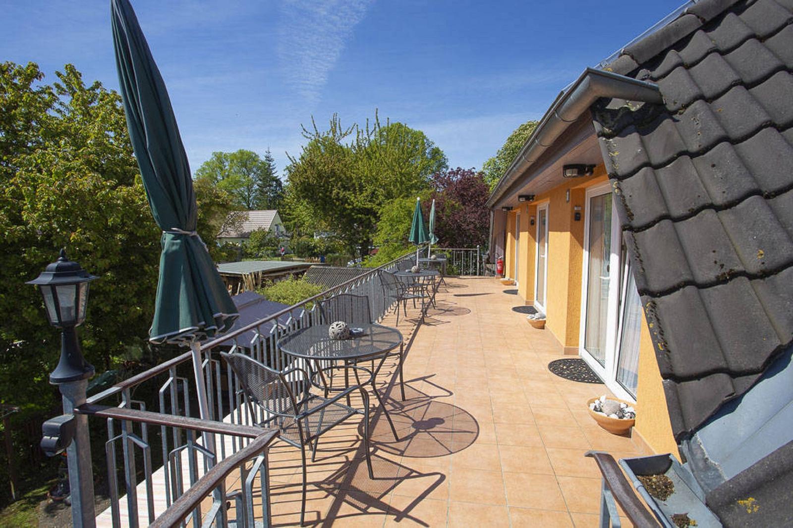 Terrasse mit Tischen, Stühlen und geschlossenen Sonnenschirmen neben einem gelben Haus.