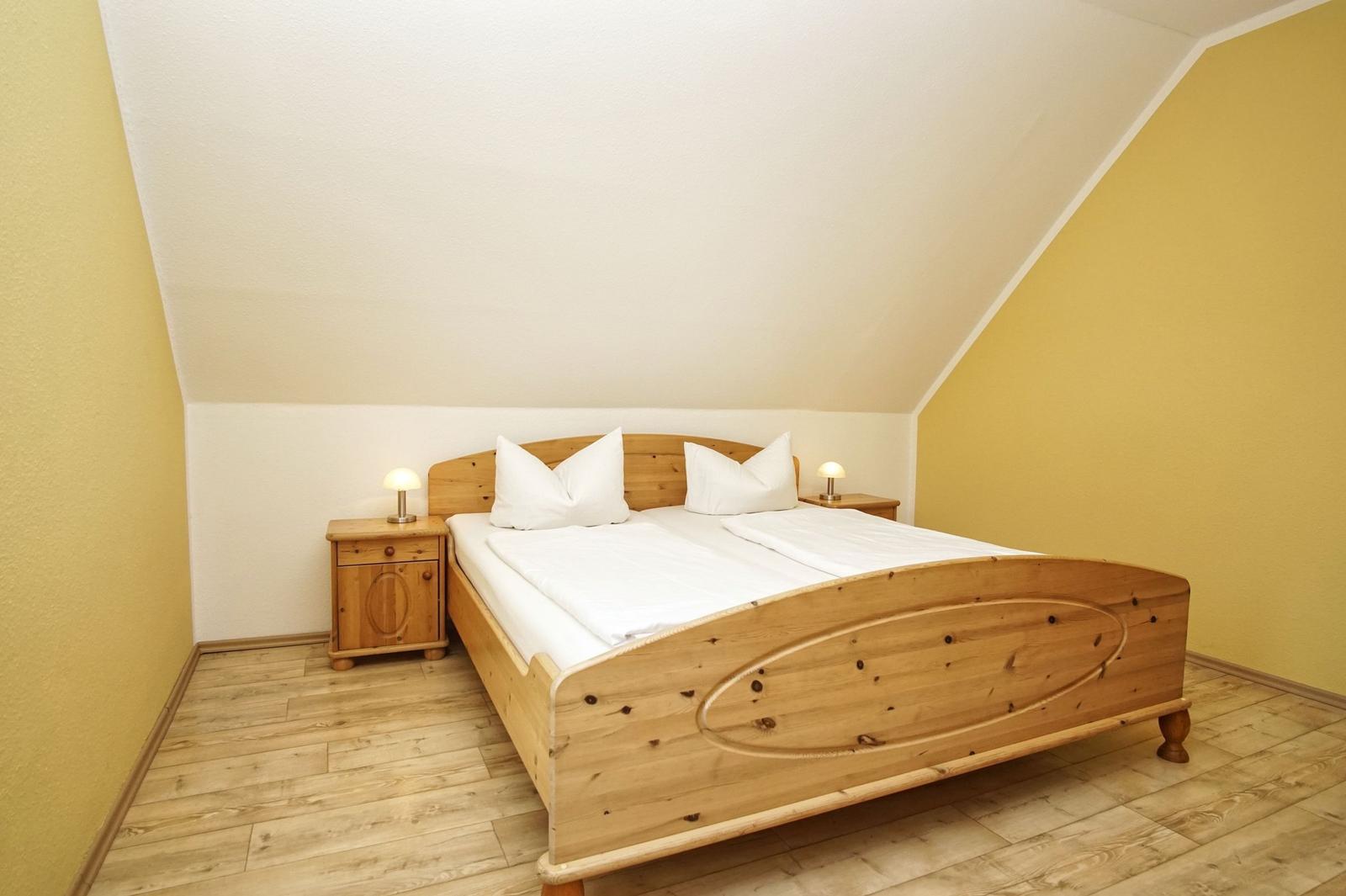 Schlafzimmer mit Holzbett, Nachttischen und Lampen unter schrägem Dach.