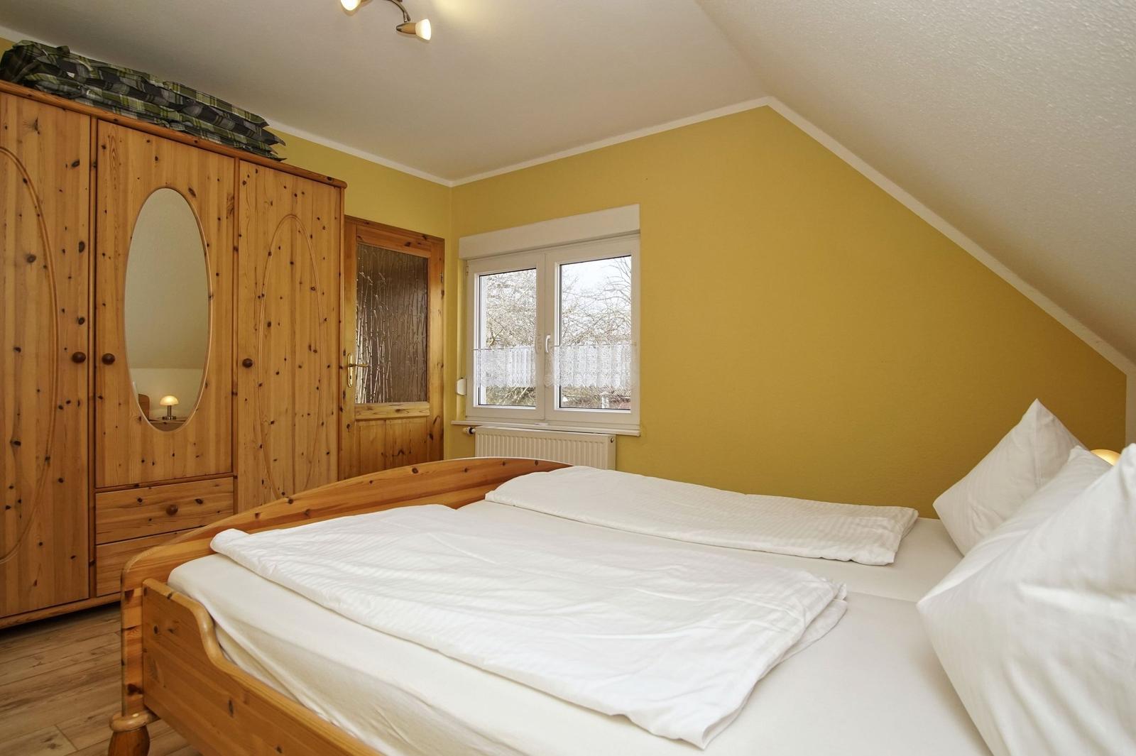 Schlafzimmer mit Holzbett, Kleiderschrank und Fenster.