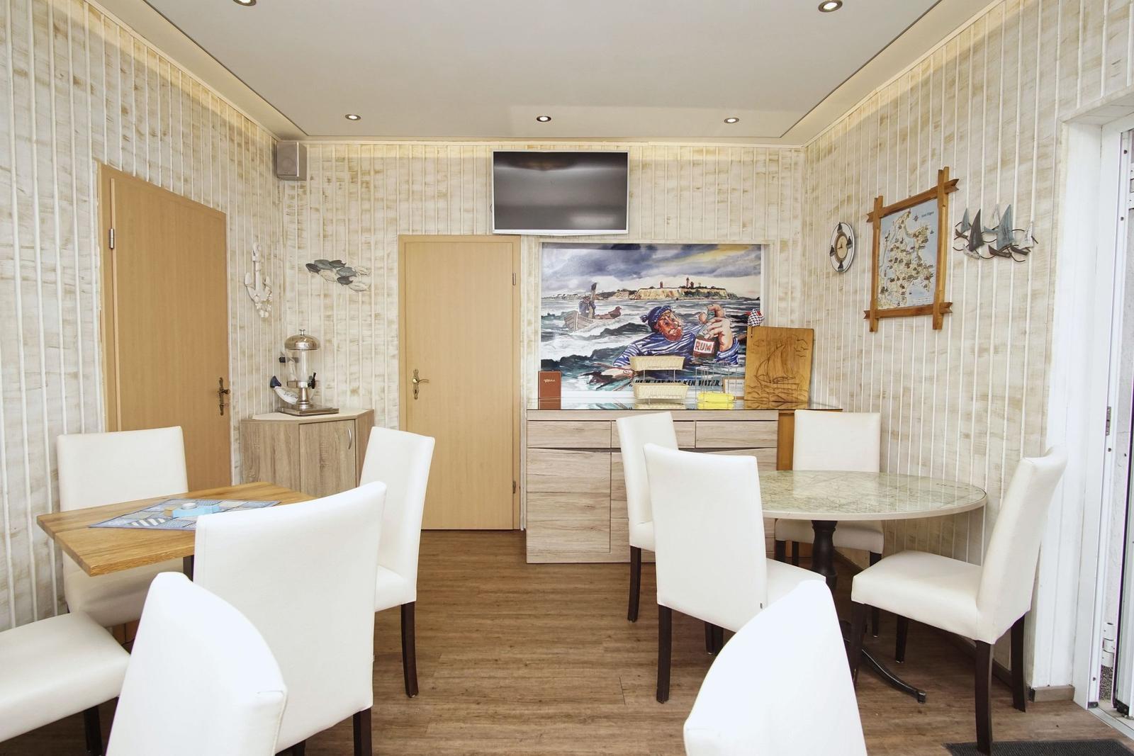 Esszimmer mit zwei Tischen, weißen Stühlen und Wandbildern. Holzfußboden und vertikale Wandverkleidung.