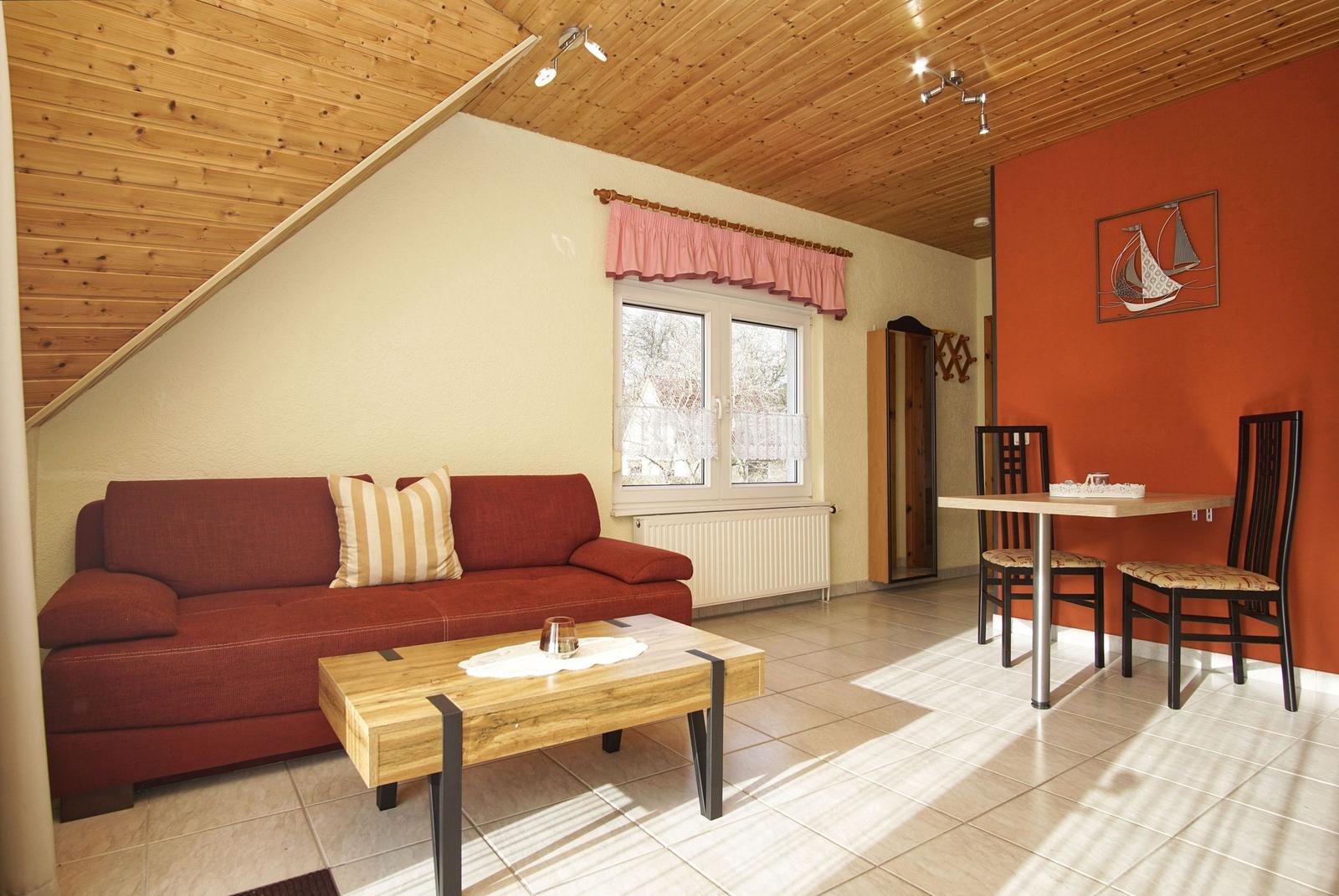 Wohn- und Essbereich mit Sofa, Tisch und Stühlen unter Holzdecke.