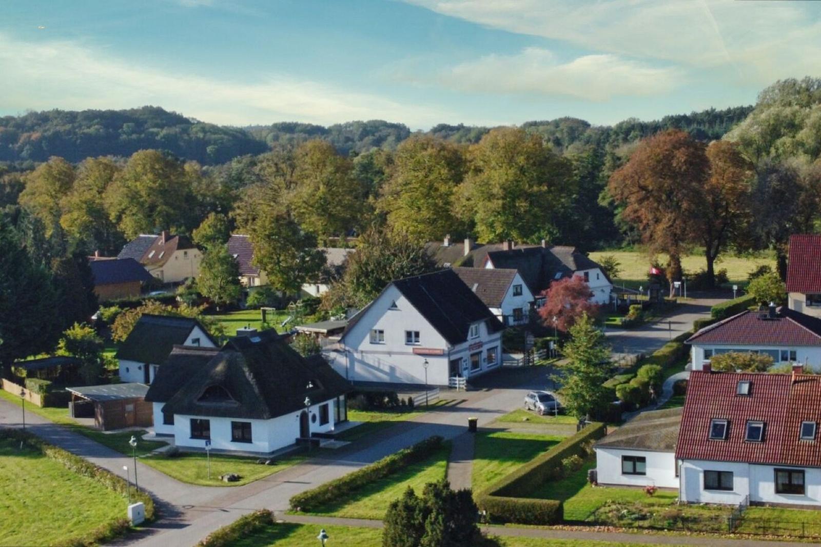 Dorf mit weißen Häusern und grünen Wiesen unter blauem Himmel.