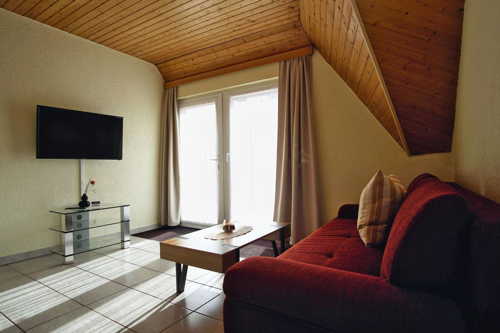 Wohnzimmer mit rotem Sofa, Fernseher und Fenster mit Vorhängen.