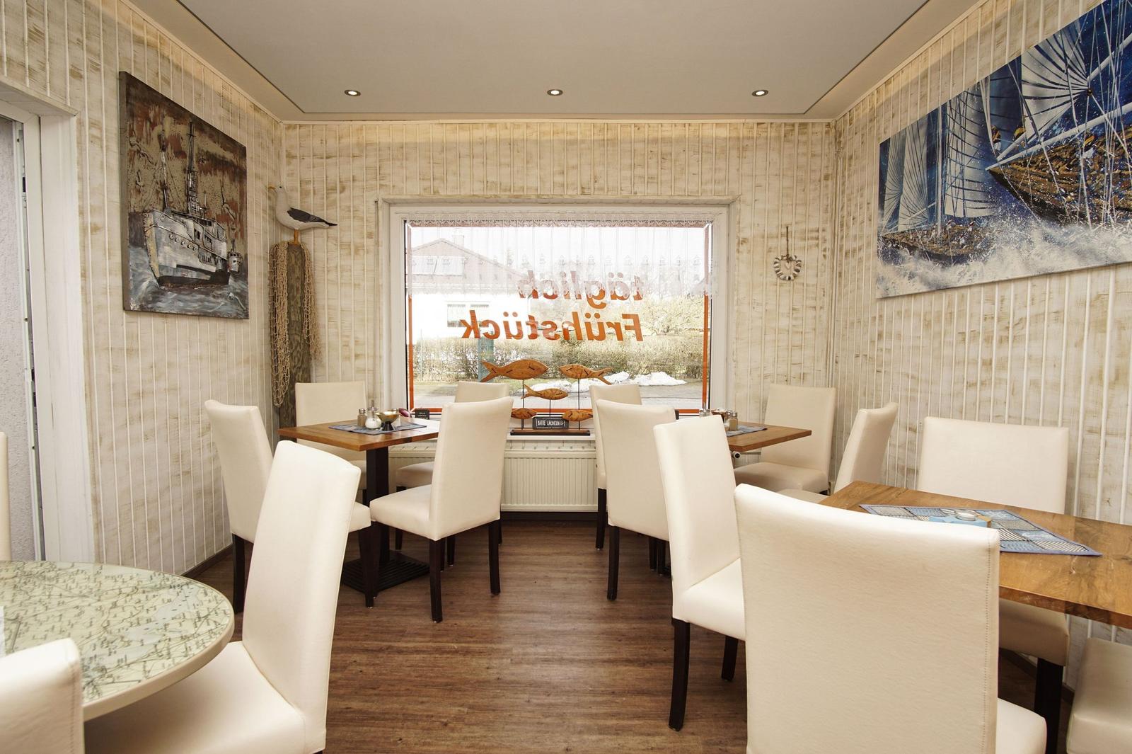 Esszimmer mit Holztischen, weißen Stühlen und maritimen Wandbildern.