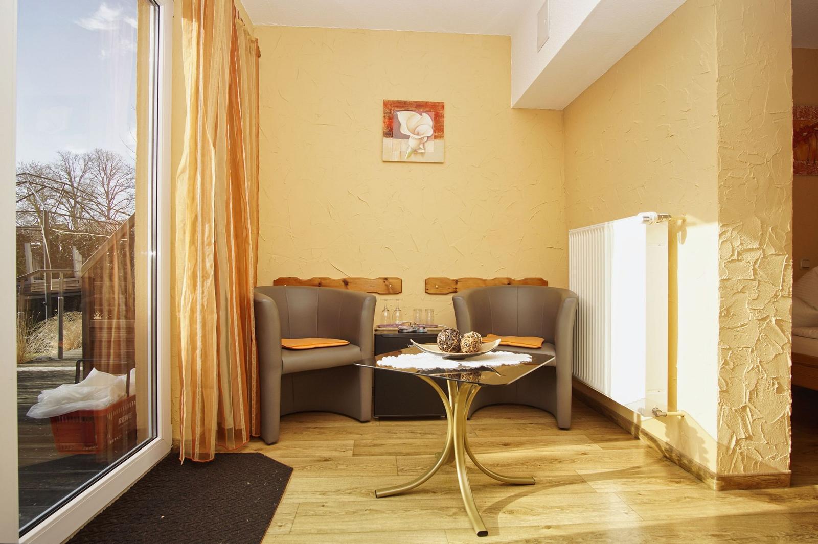 Zimmer mit zwei Sesseln, Tisch und Fenster zur Terrasse.