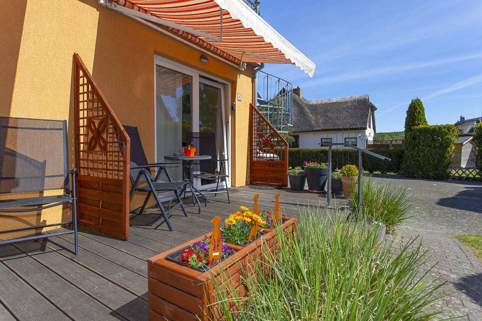 Terrasse mit Sitzgelegenheiten und Blumenbeeten vor einem gelben Haus.