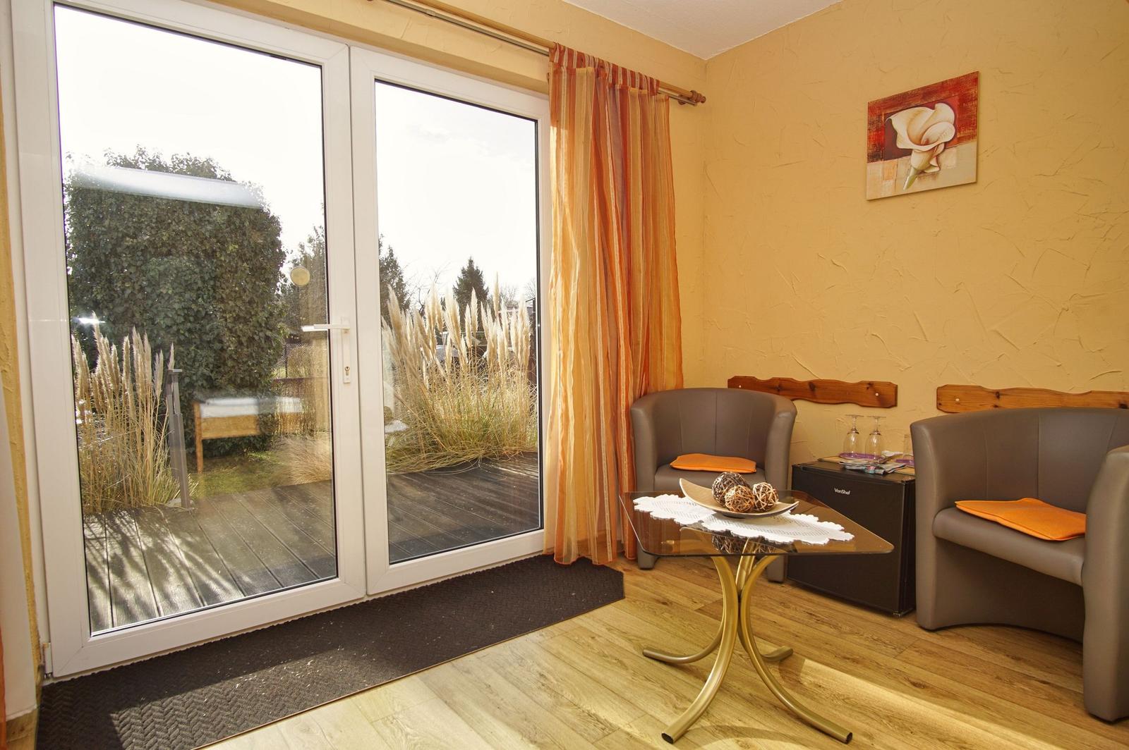 Zimmer mit zwei Sesseln, Tisch und Blick auf Balkon mit Pflanzen.