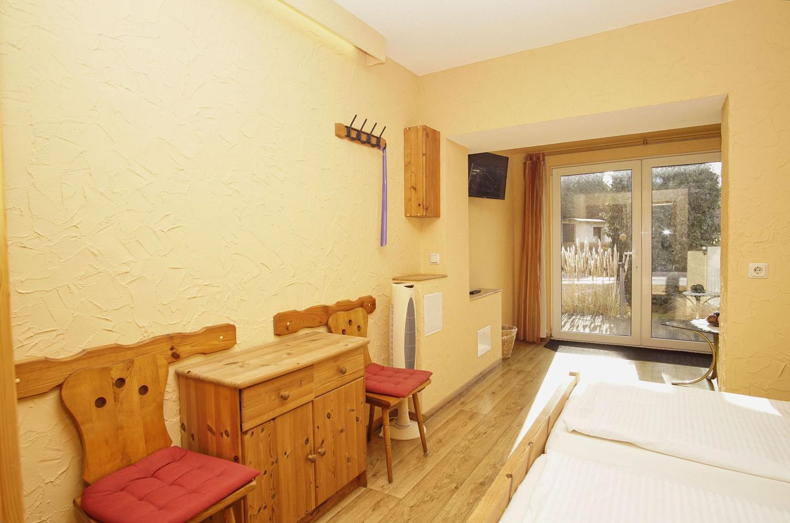 Zimmer mit Holzmöbeln, Bett und Glastür zum Balkon.