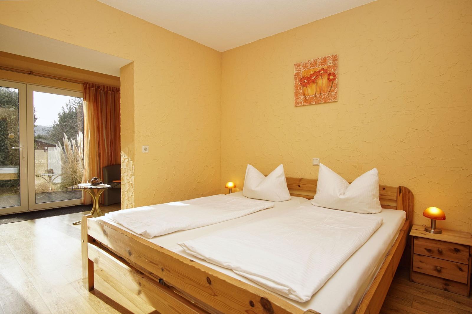 Schlafzimmer mit Doppelbett, Holzmöbel und Terrassentür.