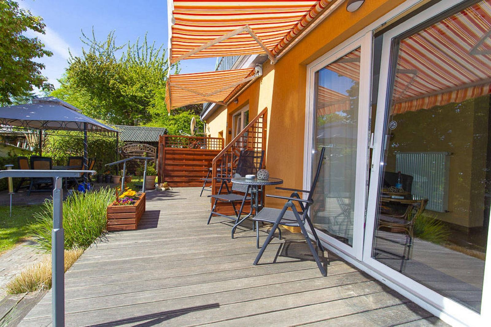 Terrasse mit Sitzgruppe unter orangefarbenem Markisenüberdachung. Holzdecke und Garten im Hintergrund.