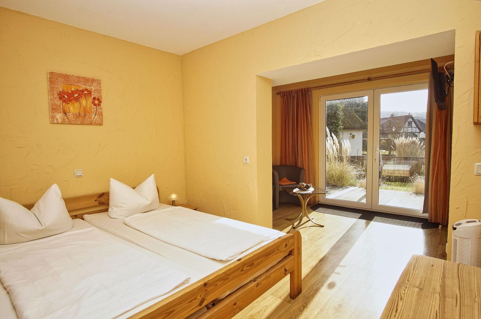 Schlafzimmer mit Doppelbett, Holzboden und Balkon mit Gartenblick.
