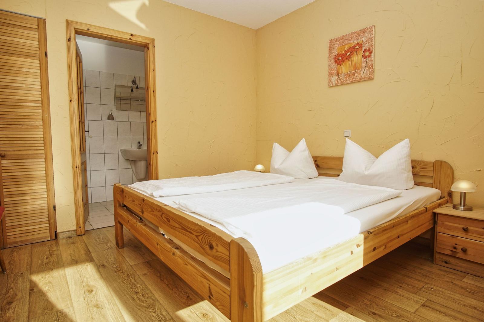 Schlafzimmer mit Holzbett, Nachttisch und Tür zum Badezimmer.