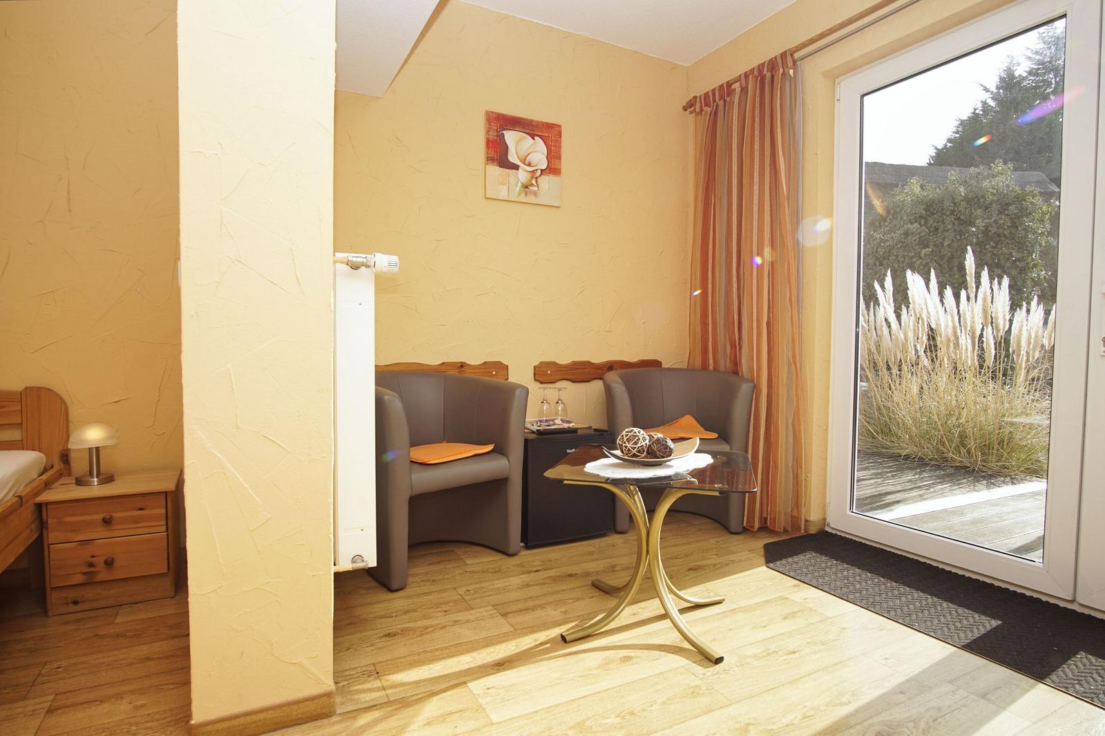 Zimmer mit Sitzbereich, Schlafplatz und Glastür zum Balkon.