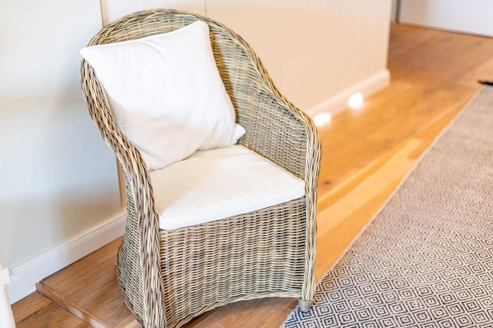 Ein geflochtenes Sitzmöbel mit weißer Polsterung steht auf Holzboden.