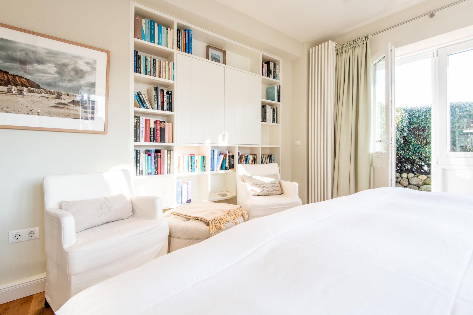 Schlafzimmer mit Bücherregal, Sitzgelegenheiten und Fenster zum Garten.